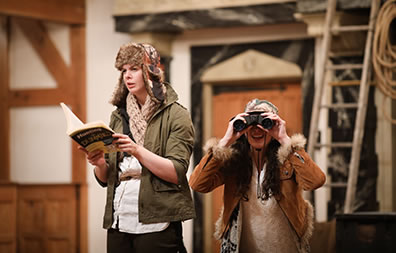 Production photo by Lindsey Walters of Pauly with Hunting for Dummies book and a crouching Her looking through binoculars